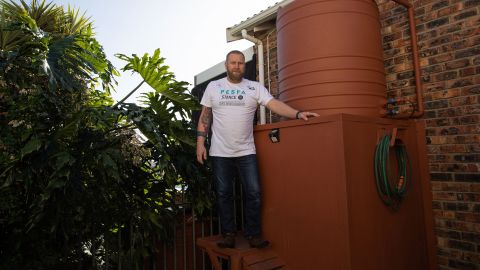 Rhett Saayman de pie junto a uno de sus varios tanques de agua en su casa en Kamma Heights.