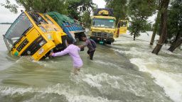 People wade past stranded trucks on a flooded street in Sunamganj in Bangladesh on June 21, 2022. 