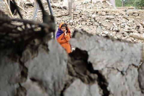 A girl stands near a house that was damaged by the earthquake.
