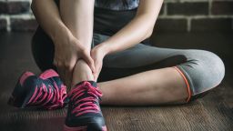 her ankle injured in gym fitness exercise training, healthy lifestyle concept, indoors wooden floor brick wall background