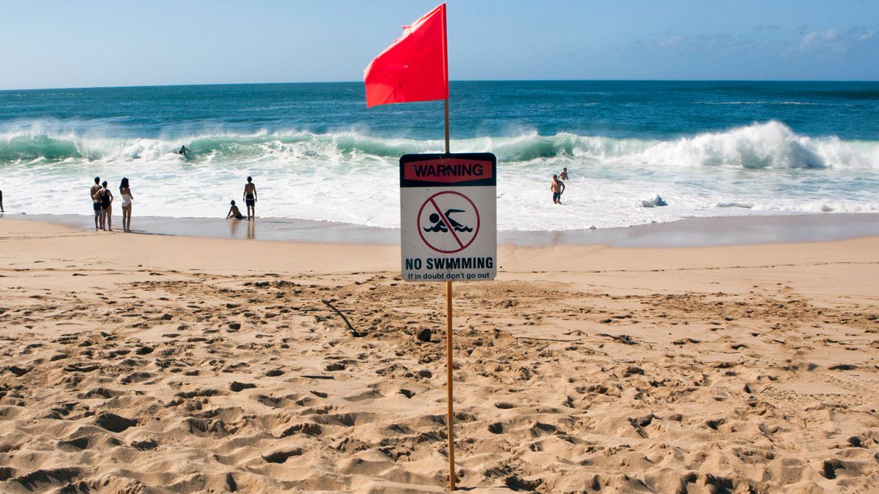 People swim in the surf at Waimea Bay Beach Park on the North Shore of Oahu, Hawaii, under a warning flag. Experts say do not underestimate the power of waves, even if there is no official warning.