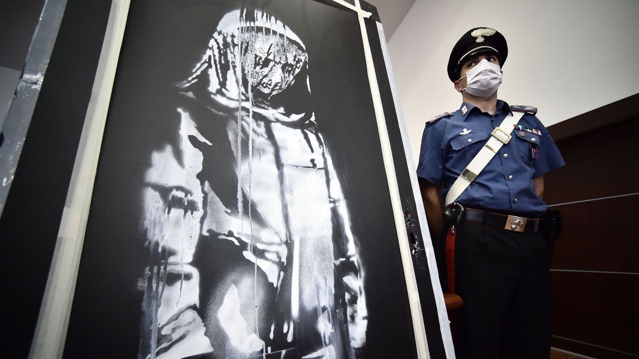 A policeman stands guard near a piece of art attributed to Banksy, that was stolen at the Bataclan in Paris in 2019, and found in Italy, ahead of a press conference in L'Aquila on June 11, 2020. - The work was found in an abandoned farmhouse in Abruzzo, l'Aquila prosecutor informed on June 10, 2020. (Photo by Filippo MONTEFORTE / AFP) / RESTRICTED TO EDITORIAL USE - MANDATORY MENTION OF THE ARTIST UPON PUBLICATION - TO ILLUSTRATE THE EVENT AS SPECIFIED IN THE CAPTION (Photo by FILIPPO MONTEFORTE/AFP via Getty Images)
