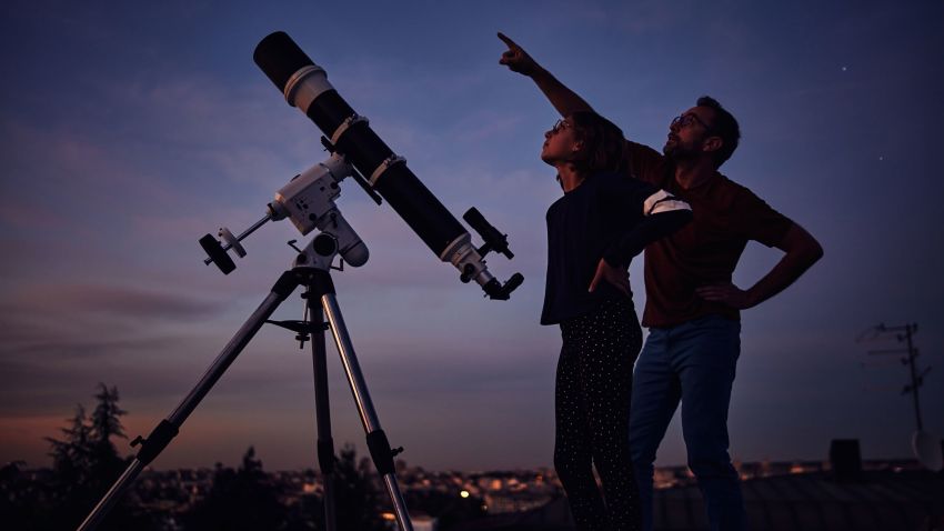 Silhouettes of father, daughter and astronomical telescope under starry skies.