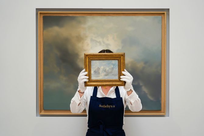 A staff member holds the painting 'Cloud Study' by John Constable in front of a painting titled 'Study for Clouds' by Gerhard Richter at Sotheby's in London on Wednesday, June 22.