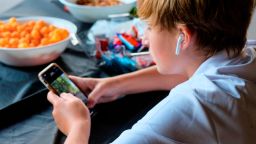 Preteen boy concentrating on smartphone with ear buds and bowls of snacks. (Photo by: Kurt Wittman/UCG/Universal Images Group via Getty Images)