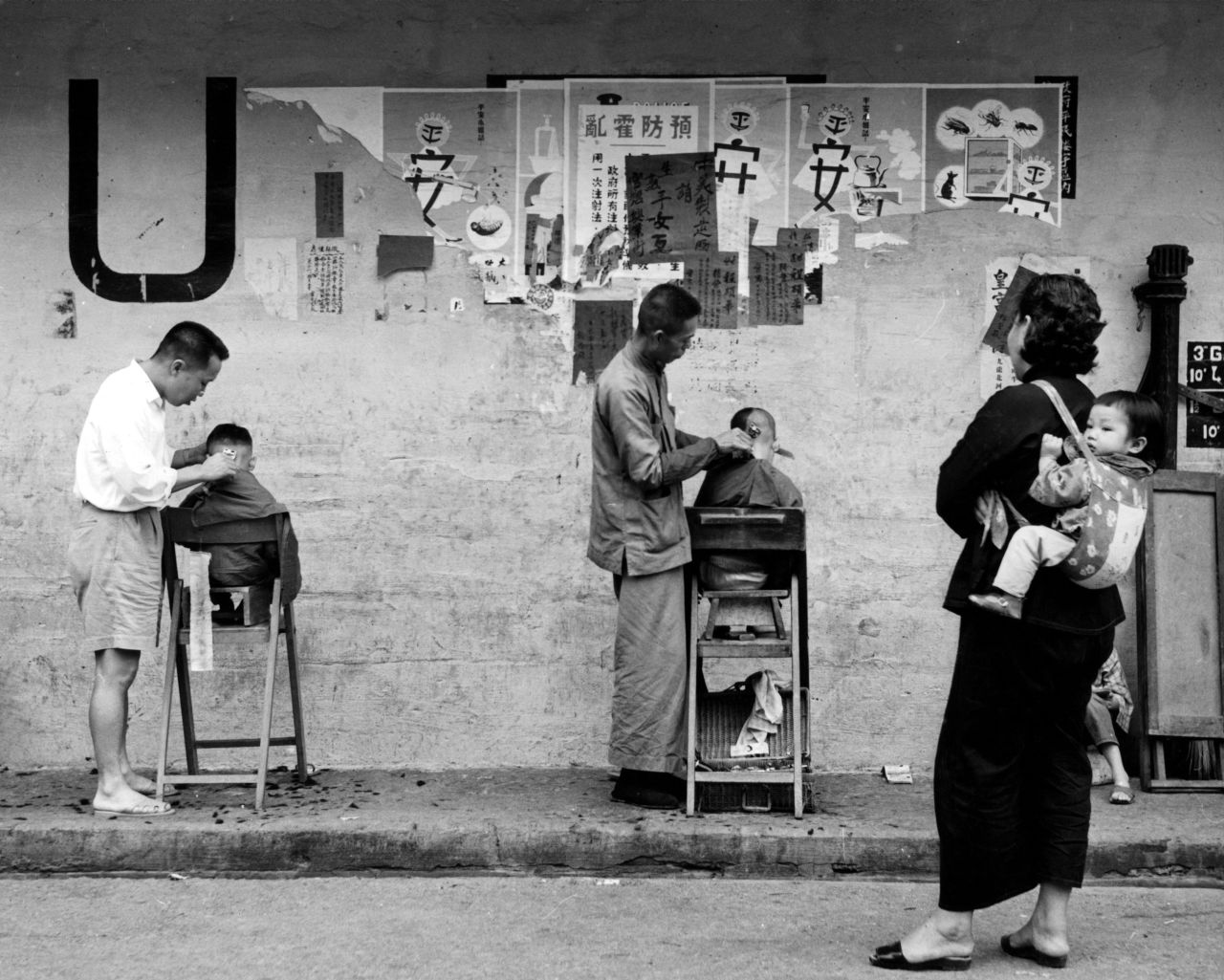 Barbers cut the hair of two boys on a street in Hong Kong.