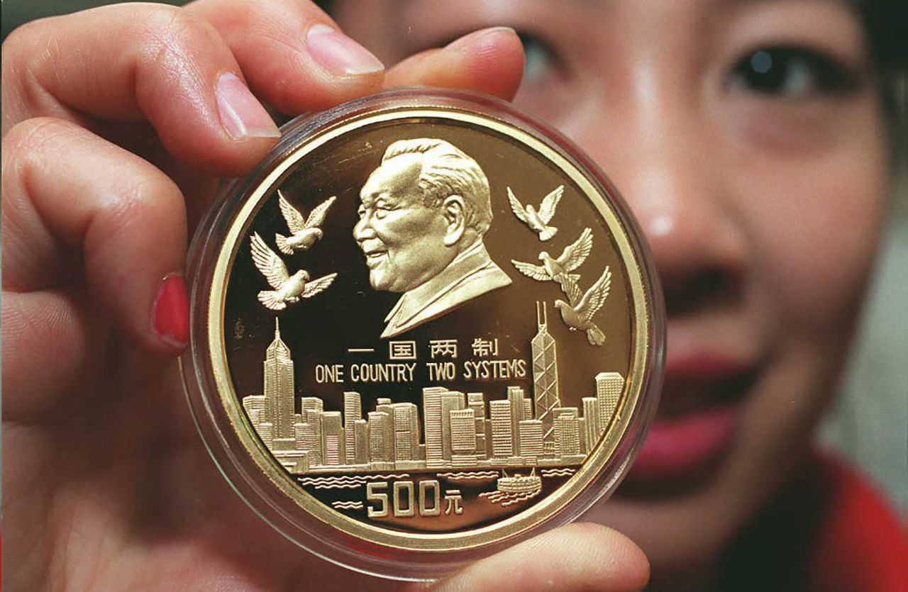 An employee of the China Gold Coin Corporation displays a 99.99% pure gold coin issued by the People's Bank of China to commemorate the handover of Hong Kong to China. It features a portrait of China's paramount leader Deng Xiaoping, the Hong Kong skyline and the inscription "One Country Two Systems."