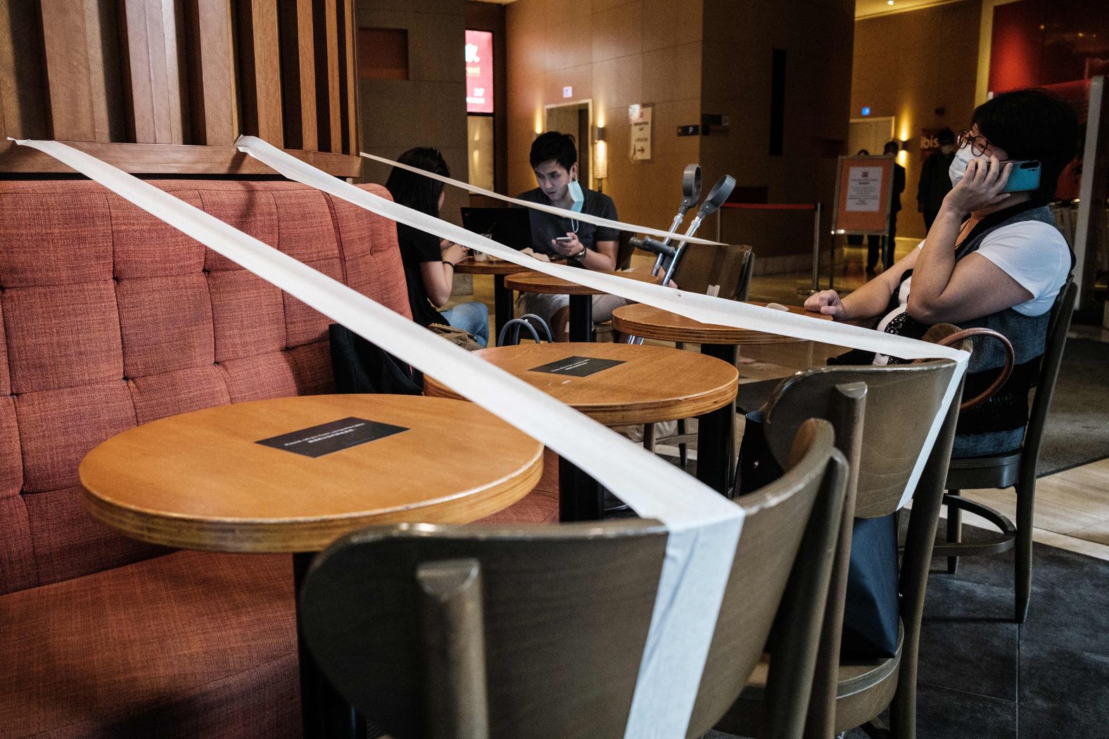 Customers wearing face masks sit in a Hong Kong cafe that had masking tape on every other table to enforce social distancing in 2020.