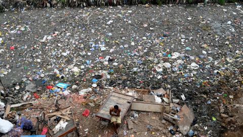 A man sits on a cart next to a sewer canal filled with plastics and other waste in New Delhi on June 30, 2022. 