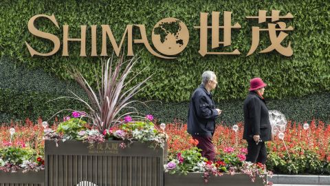 An elderly couple walk past a sign in front of Shimao Tower, developed by Shimao Group Holdings Ltd., in Shanghai, China, on Saturday, Jan. 8, 2022.