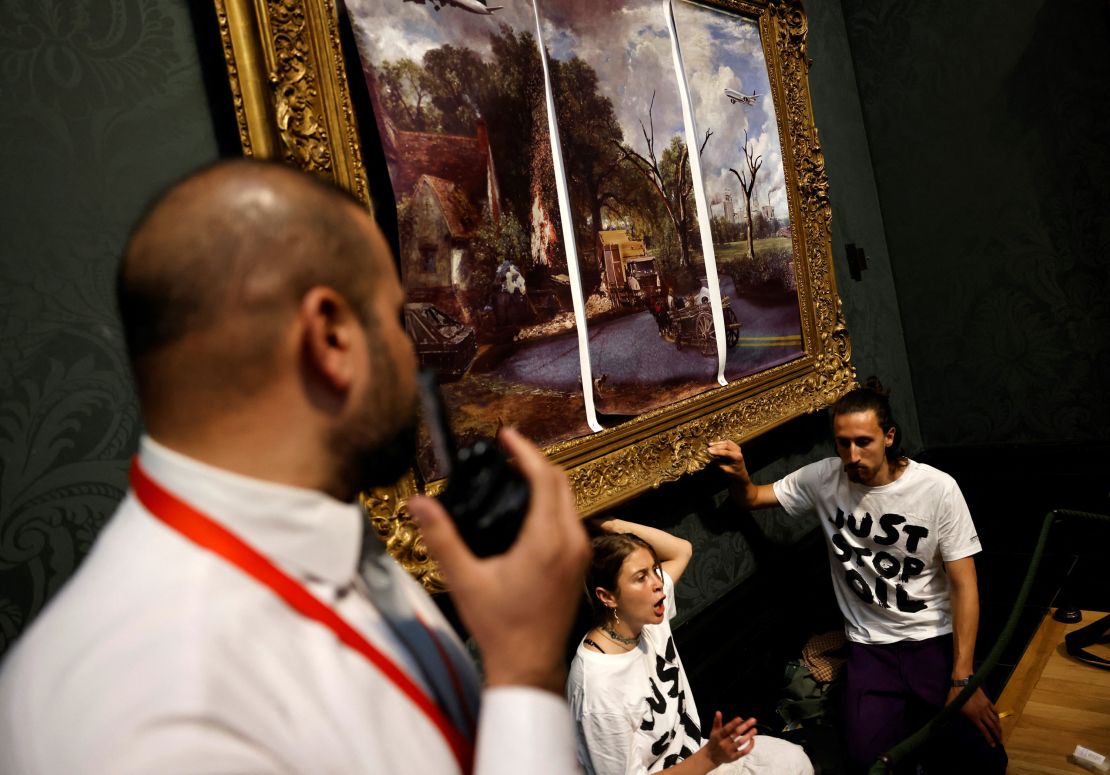 Just Stop Oil activists glue their hands to the frame of John Constable's "The Hay Wain," which was also covered by posters reimagining the scene, in London's National Gallery on July 4, 2022.