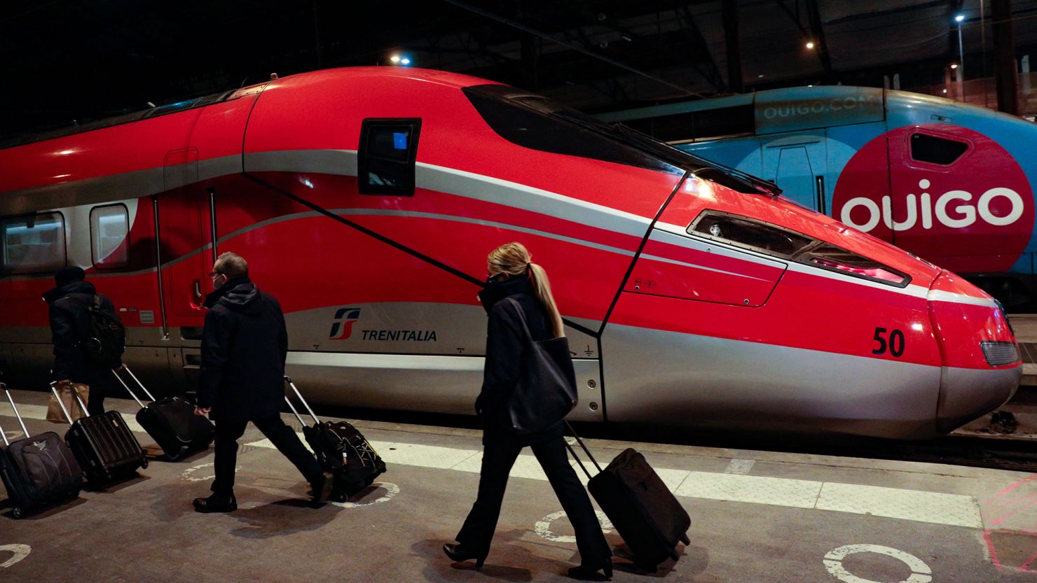 Travelers pull their luggage past an Italian high-speed Frecciarossa, a high-speed train of the Italian national train operator, Trenitalia.