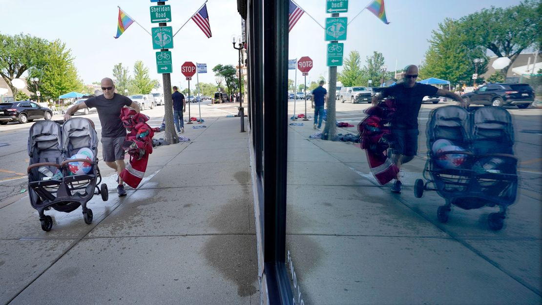 Highland Park resident Murry Rosenbush is reflected in a store window Tuesday as he removes items left behind by attendees to the town's Fourth of July parade.