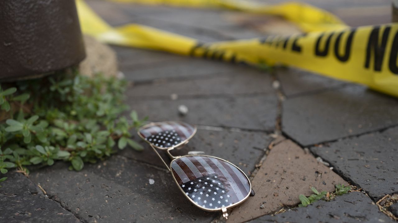 Police crime tape is seen near an American flag-themed sunglasses laying on the ground at the scene of the Fourth of July parade shooting in Highland Park, Illinois on July 4, 2022. 