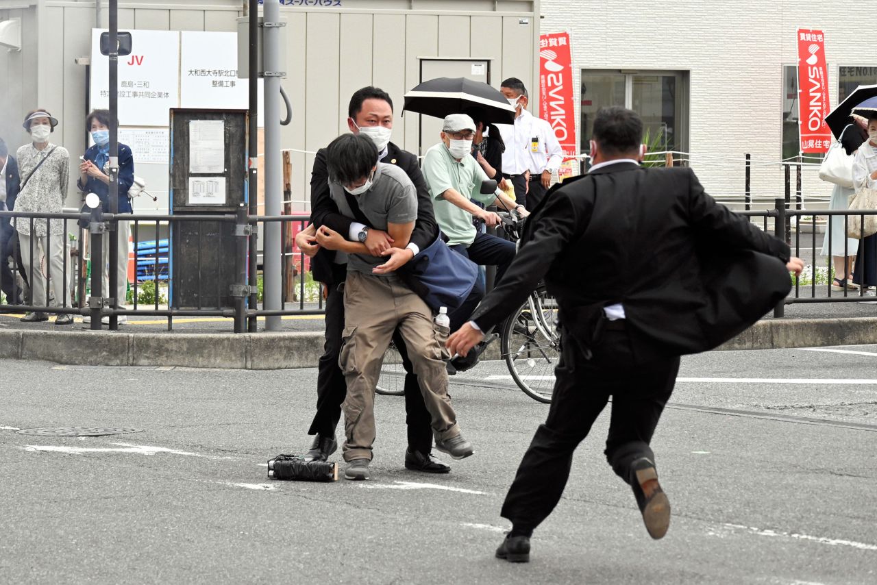 Security police tackle a suspect who was believed to have shot Japanese Prime Minister Shinzo Abe in Nara, Japan, on Friday, July 8. What appears to be a handmade gun lies on the ground as a security officer seizes the suspect.