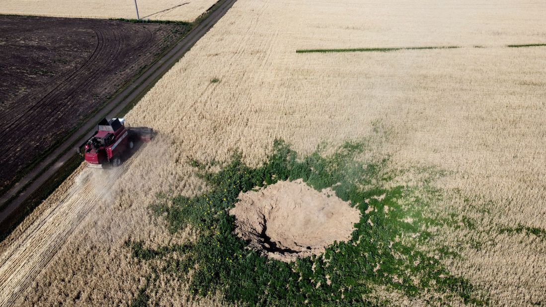 A farmer drives a combine harvester past a crater suspected to be caused by an air strike near Kramatorsk, Ukraine, on July 7.