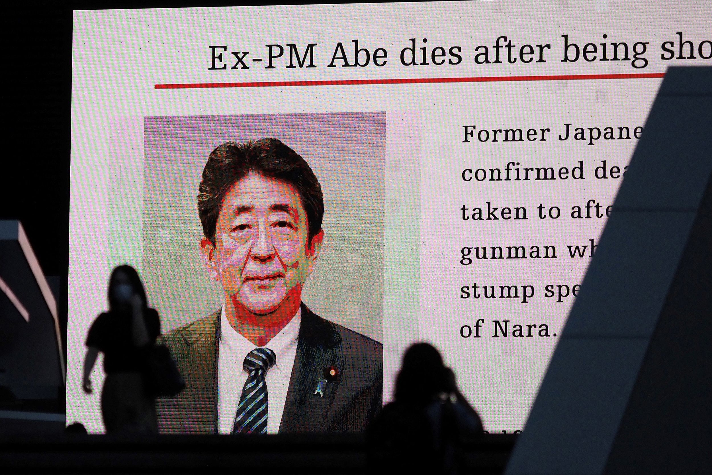 People are silhouetted against a video screen in Tokyo showing news of Abe's death.