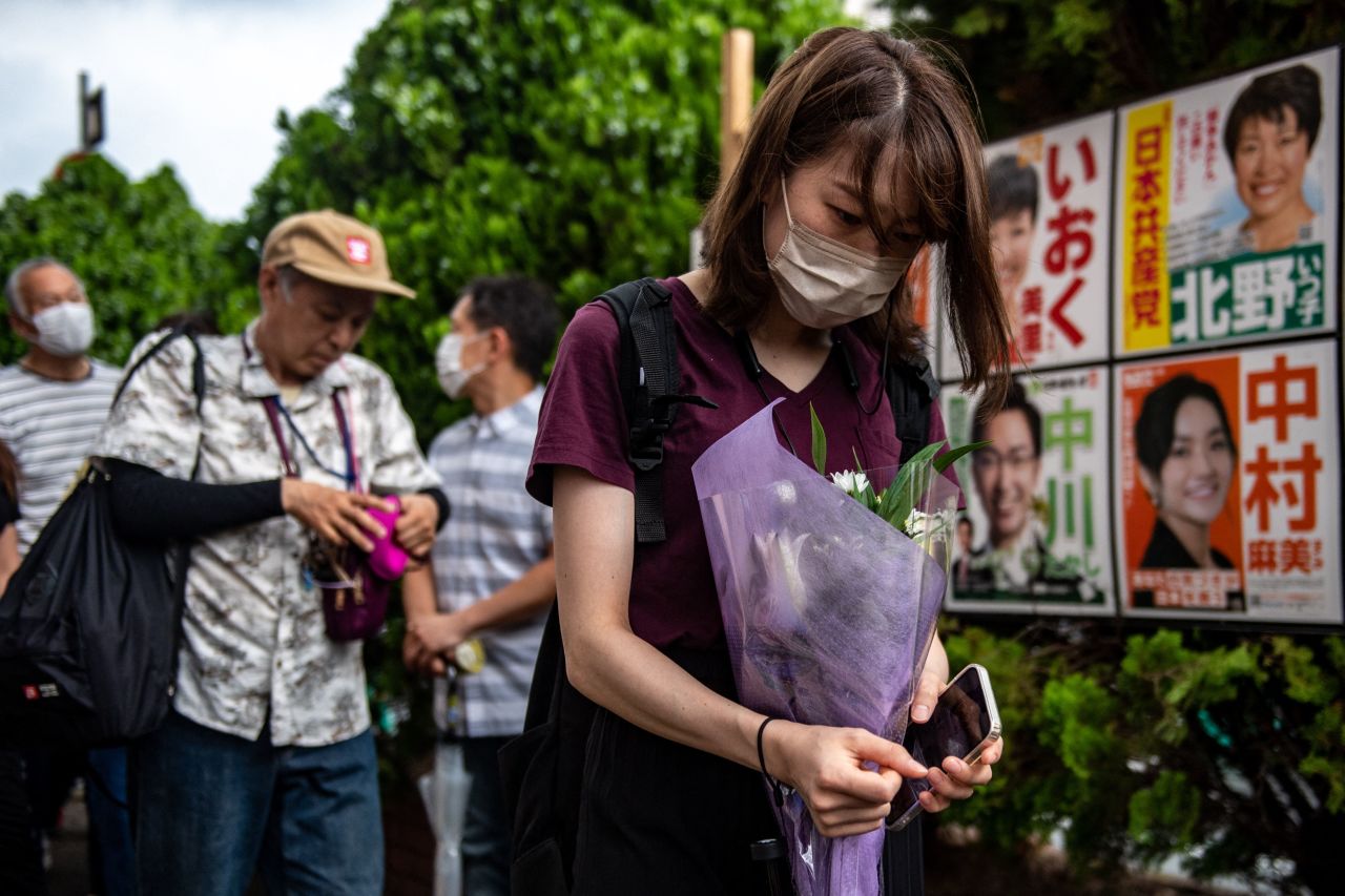 People line up to place flowers at a makeshift memorial where Abe was shot on Friday.