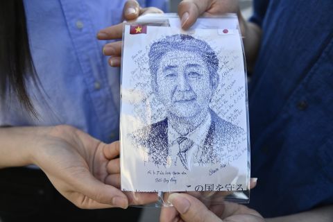A couple show an illustration of Shinzo Abe as they pay homage in front of his residence in Tokyo, Japan, on July 10.