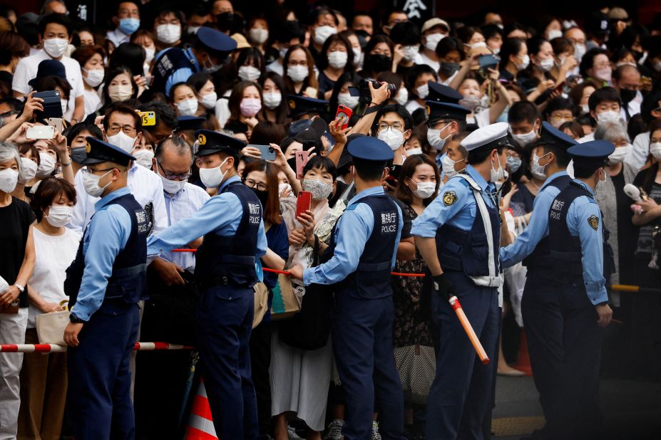 Police officers stand guard as people watch a motorcade carrying the body of the late former Japanese Prime Minister Shinzo Abe in Tokyo, Japan, on July 12.