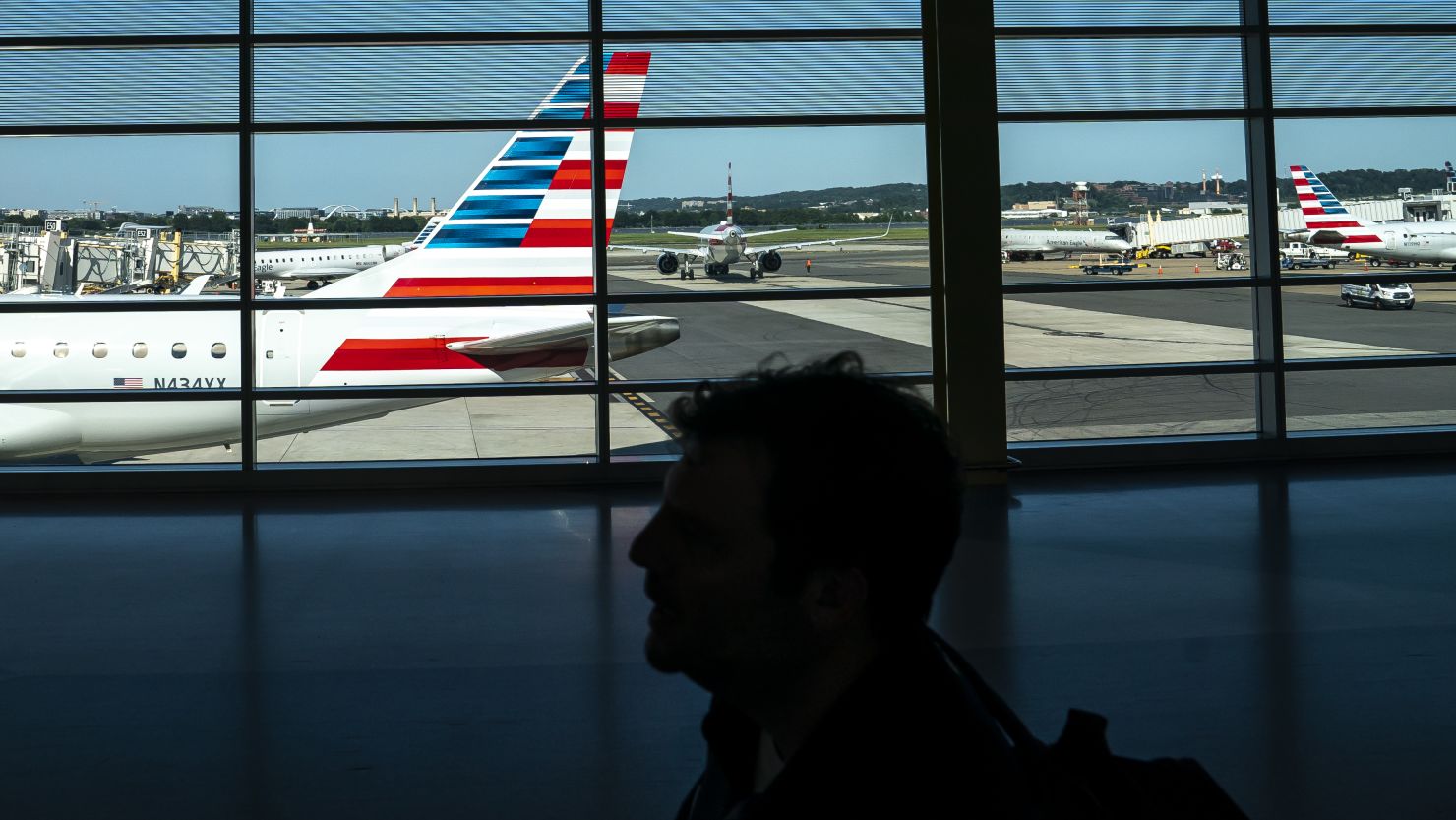 ARLINGTON, VA - JULY 11: A traveler walks past American Airlines planes gated at Ronald Regan Washington National Airport on July 11, 2022 in Arlington, Virginia. Staffing shortages, the COVID-19 pandemic and other issues have led to historic levels of disruptions in U.S. air travel. (Photo by Nathan Howard/Getty Images)