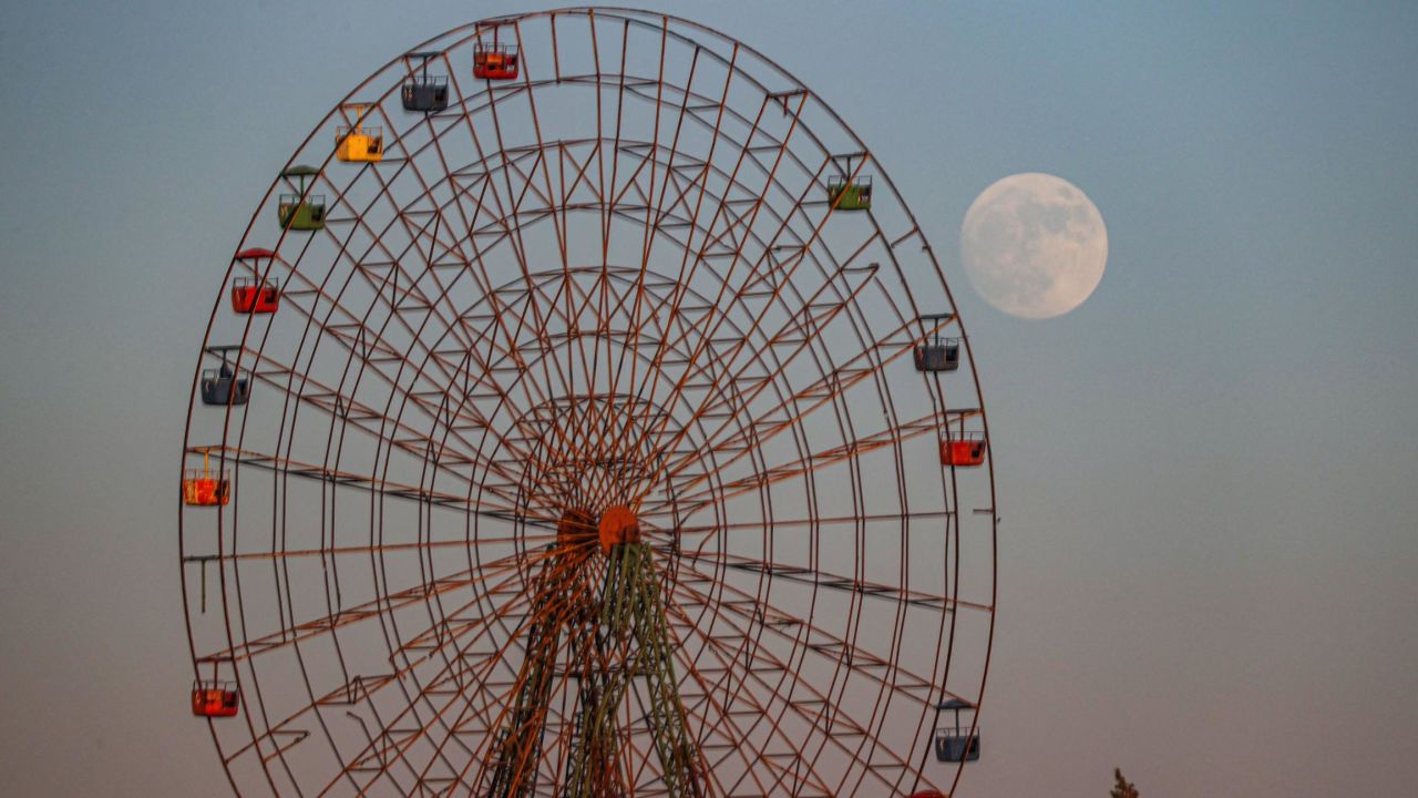The moon rises behind a rundown Ferris wheel at an abandoned children's amusement park near al-Nayrab, a village ravaged by pro-government forces bombardment, in Syria's northwestern Idlib province on July 12, 2022 a day ahead of the July "buck supermoon".