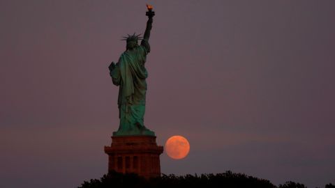 The moon rises behind the Statue of Liberty in New York City on July 12, 2022 as seen from Jersey City, New Jersey.  