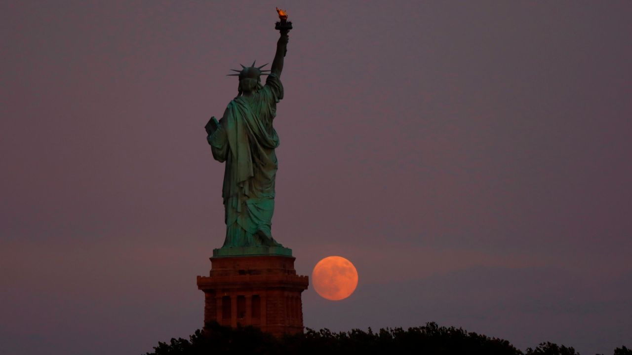 The moon rises behind the Statue of Liberty in New York City on July 12, 2022 as seen from Jersey City, New Jersey.
