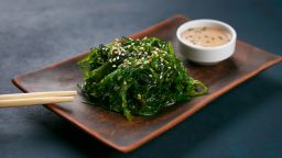 Delicious Japanese cuisine, wakame chuka salad with spicy sauce served on authentic square clay plate, close up. Healthy vegetarian seafood