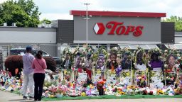 Community members pay respects at a "Memorial Garden" filled with flowers, photos and mementos outside the Tops Friendly Market on Jefferson Avenue on July 14, 2022 in Buffalo, New York. The store was the scene of a mass shooting on May 14, 2022 when accused shooter Payton Gendron killed 10 Black people and injured three others in what is believed to be a racially-motivated attack. The market will reopen to the public Friday after extensive renovations to the building.