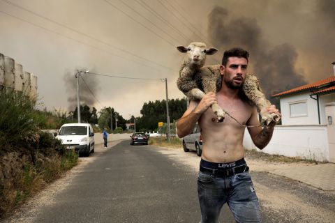 A man carries a sheep on his back as a wildfire burns in Boa Vista, Portugal, on Tuesday, July 12. <a href="https://www.cnn.com/2022/07/12/world/heat-wave-rare-alerts-europe-intl/index.html" target="_blank">Extreme heat</a> has been making wildfires worse in Portugal and other parts of southwestern Europe.