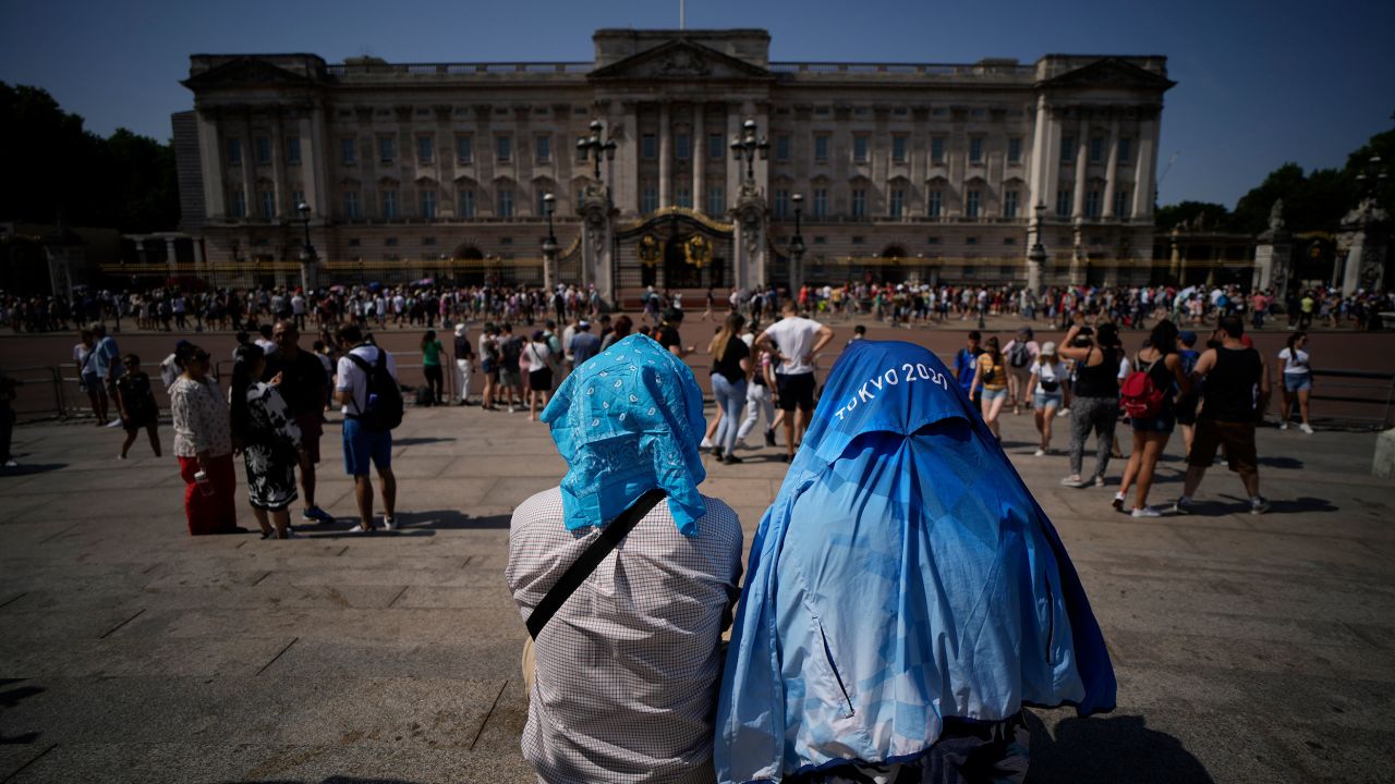 People shield their heads from the sun on Monday after a scaled down version of the Changing of the Guard ceremony took place outside Buckingham Palace in London during an extreme heat wave.