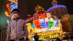 People wearing protective masks walk in front of the Casino Lisboa, operated by SJM Holdings Ltd., at night in Macau, China, on Tuesday, March 3, 2020. Casinos in Macau, the Chinese territory that's the worlds biggest gambling hub, reported a record drop in gaming revenue, as they grappled with the cost of closing down their businesses for 15 days to help contain the deadly coronavirus outbreak. Photographer: Billy H.C. Kwok/Bloomberg via Getty Images