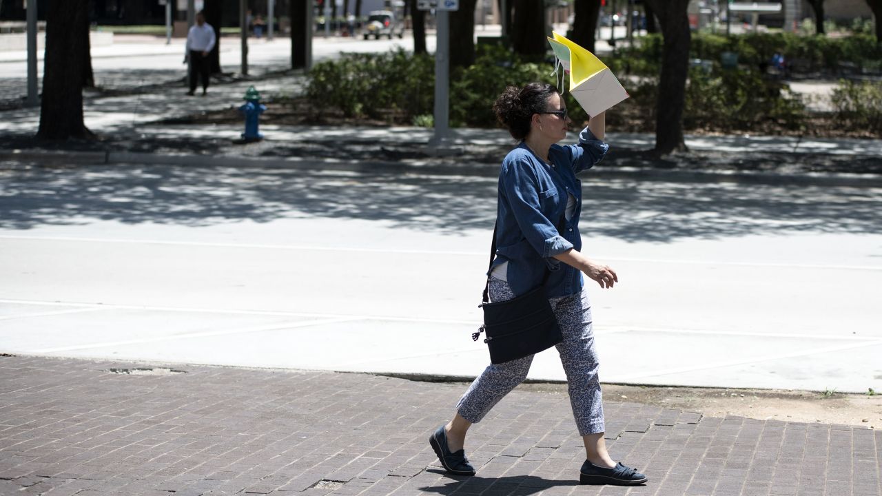 A pedestrian walks with a bag covering her face to block the sun during a heatwave in Houston, Texas. 