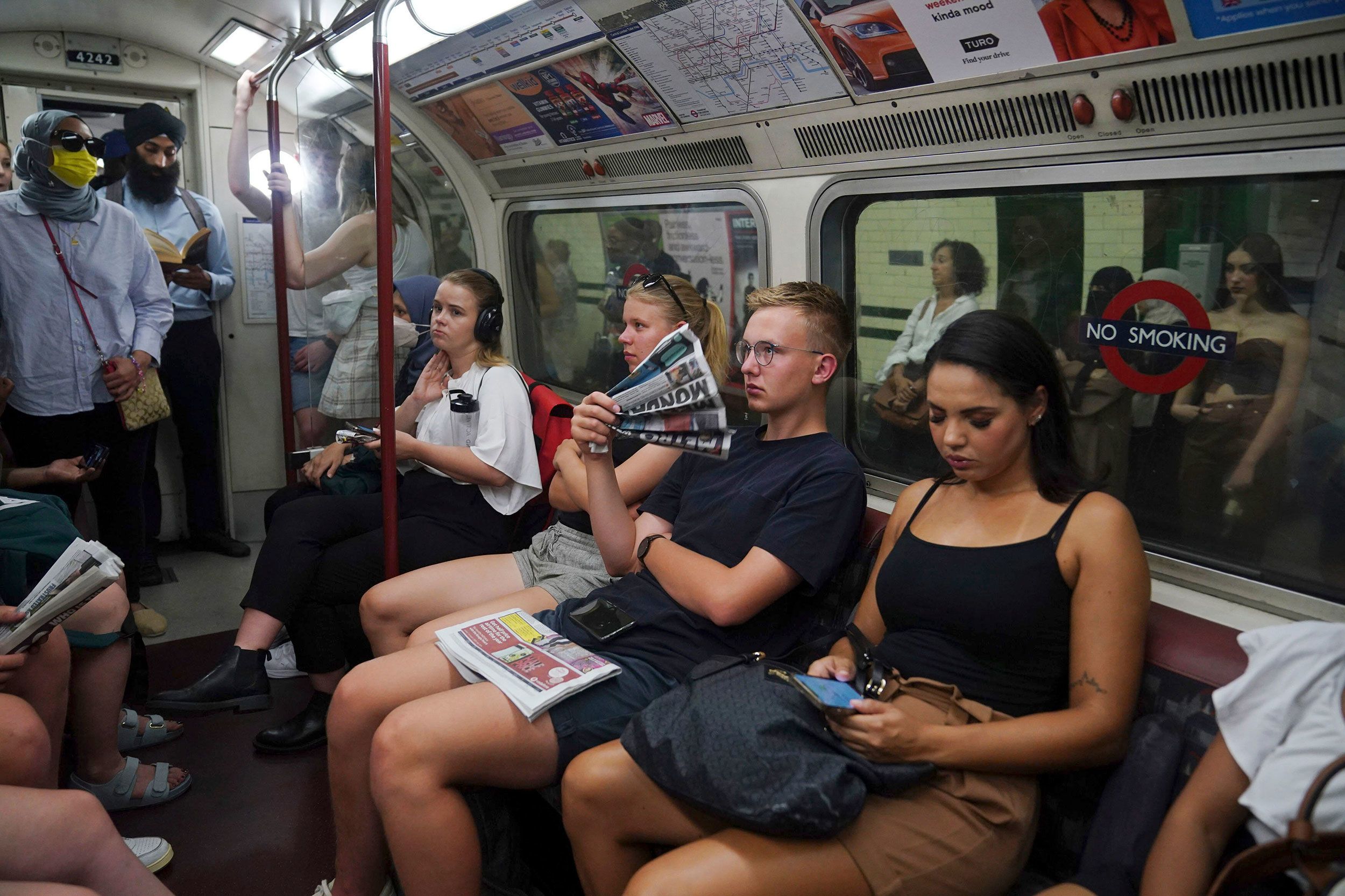 A man fans himself with a newspaper whilst traveling on a metro train in London on Monday, July 18.