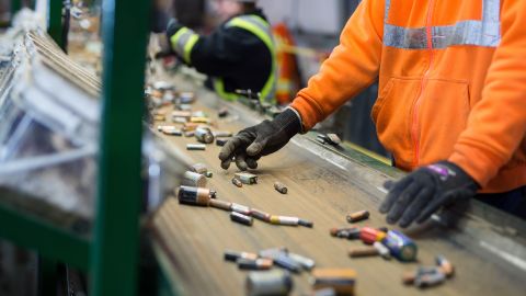 Employees sort batteries moving along a conveyor belt at a recycling facility.