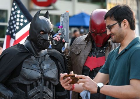 Un asistente muestra su teléfono a los cosplayers disfrazados de Batman y Red Hood el 21 de julio.