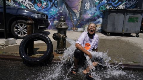 Sylvia Carrasquillo reacts as she sits in front of an open fire hydrant Friday in The Bronx neighborhood of New York City.