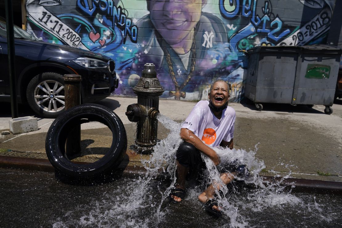 Sylvia Carrasquillo reacts as she sits in front of an open fire hydrant Friday in The Bronx neighborhood of New York City.