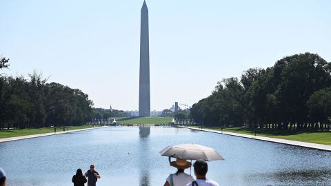 Le persone usano un ombrello per proteggersi dal sole mentre guardano il Monumento a Washington a Washington, DC, sabato.