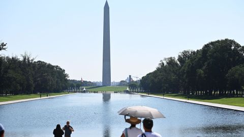 People use an umbrella to shelter from the sun while looking at the Washington Monumnet in Washington, DC, Saturday