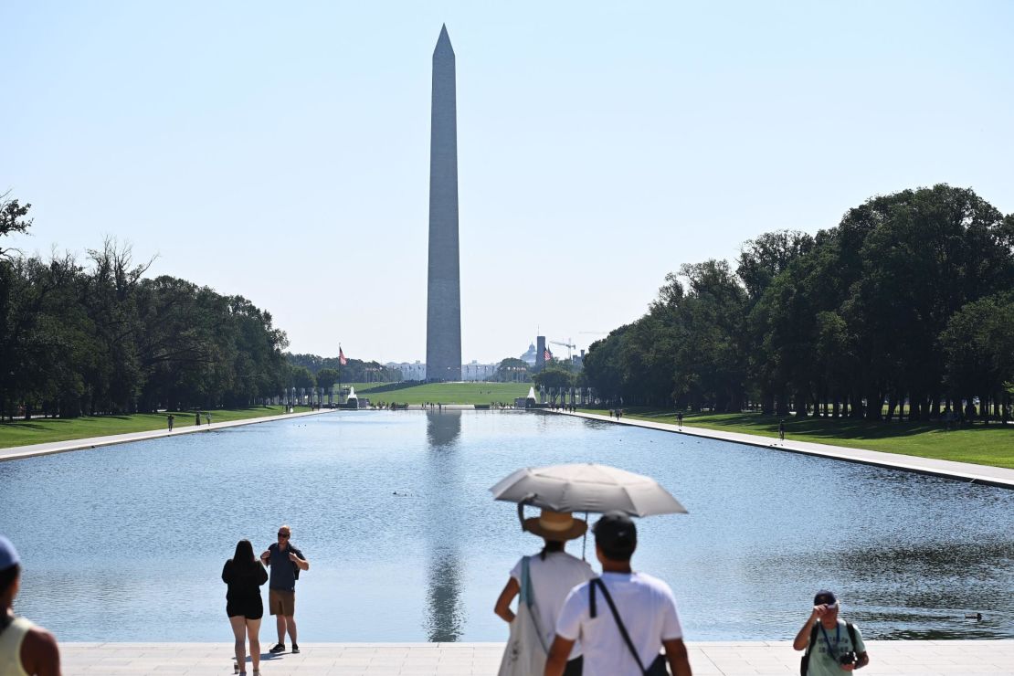 People use an umbrella to shelter from the sun while looking at the Washington Monumnet in Washington, DC, Saturday