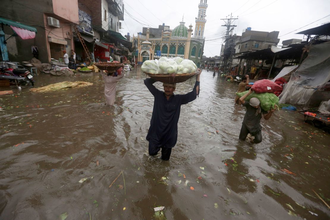 Laborers carry produce as they wade through a flooded road after heavy rainfall, in Lahore, Pakistan, Thursday, July 21, 2022. 