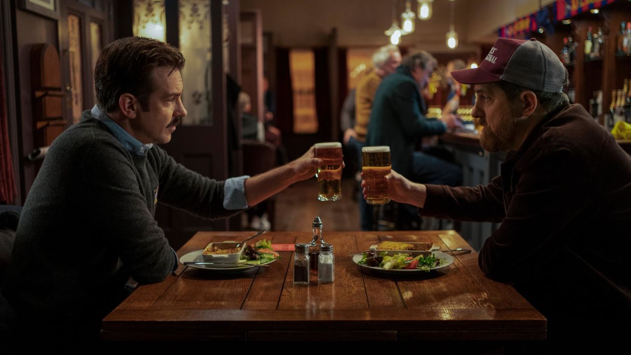 Ted Lasso (Jason Sudeikis) shares a toast with Coach Beard (Brendan Hunt) at the Crown & Anchor in an episode of "Ted Lasso."