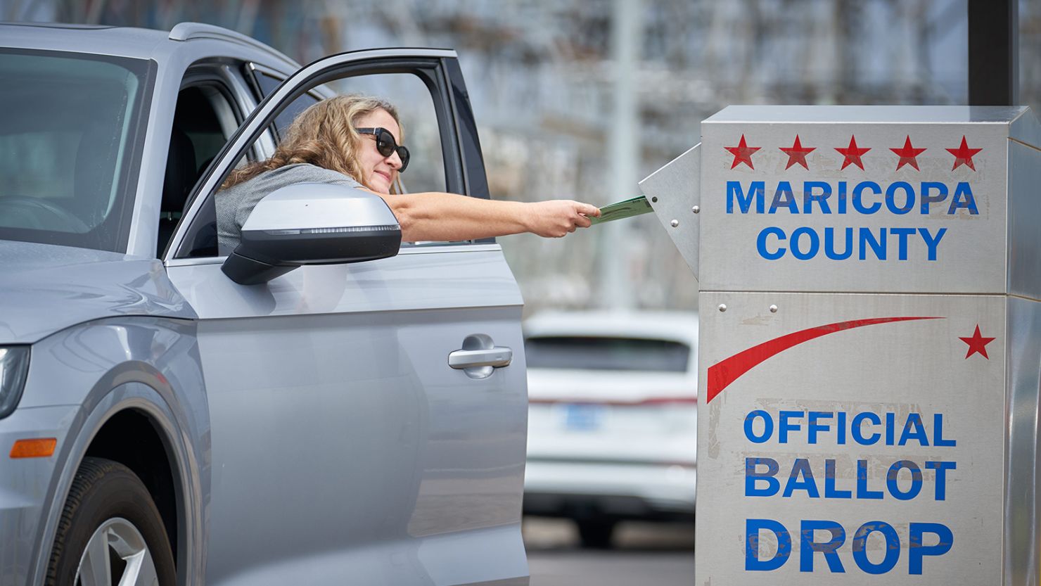 Shana Hofberger leans out of her car door to place her ballot in the ballot drop box outside the Maricopa County Tabulation and Elections Center in Phoenix for Arizona's August 2, 2022, primary election.