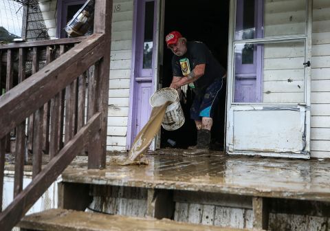 Terry Hatworth uses muddy water -- the tiny town of Garrett is without clean water currently -- to help wash off the mud on Earl Wallen's porch Friday morning, July 29.