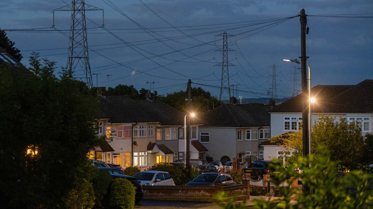 Electricity transmission towers near residential houses with lights on in Upminster, UK, on Monday, July 4, 2022. The UK is set to water down one of its key climate change policies as it battles soaring energy prices that have contributed to a cost-of-living crisis for millions of consumers.