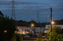 Electricity transmission towers near residential houses with lights on in Upminster, UK, on Monday, July 4, 2022. The UK is set to water down one of its key climate change policies as it battles soaring energy prices that have contributed to a cost-of-living crisis for millions of consumers. 