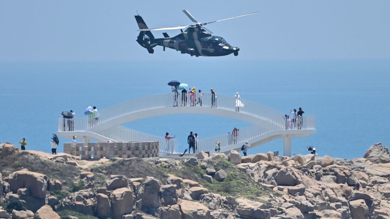 Tourists look on as a Chinese military helicopter flies past Pingtan island, one of mainland China's closest point from Taiwan  on August 4, 2022.