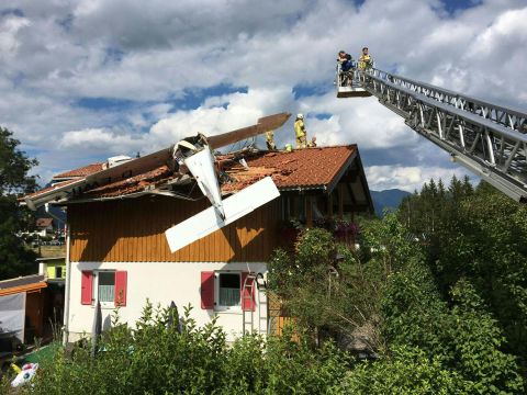 Firefighters stand on the rooftop of a house on Sunday, July 31, after a small aircraft crashed onto it in Höfen, Austria. Two people were injured.